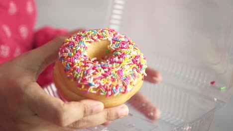 person holding a donut with sprinkles in a plastic container