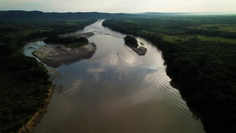 a motor boat with passengers slowly sails down the river to the horizon from the colombian hills at sunset - follow drone shot