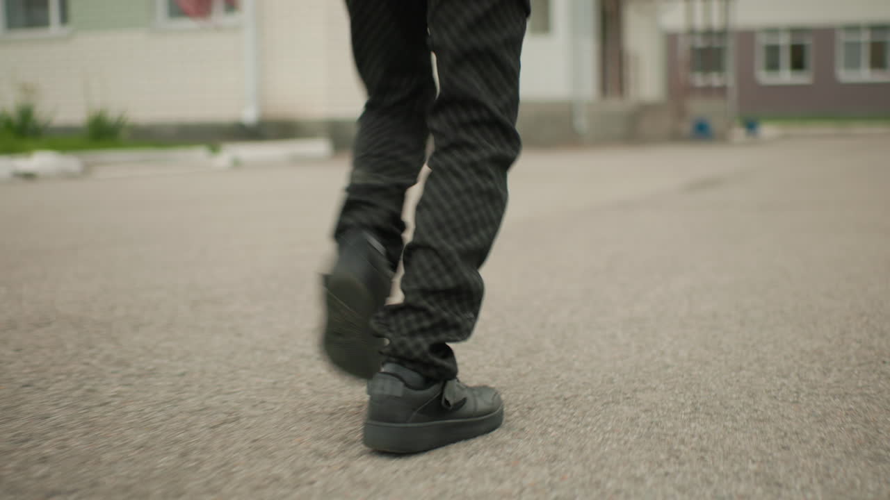 Vista en ángulo inferior de un niño con pantalones negros corriendo hacia unos escalones con marco de hierro, mostrando un movimiento decidido con enfoque en las piernas en movimiento, creando una perspectiva dinámica de un estudiante que se dirige a la escuela