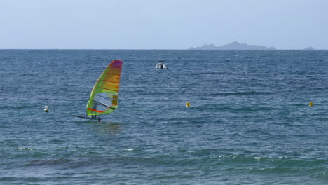 windsurfer gliding across calm ocean surface, right to left