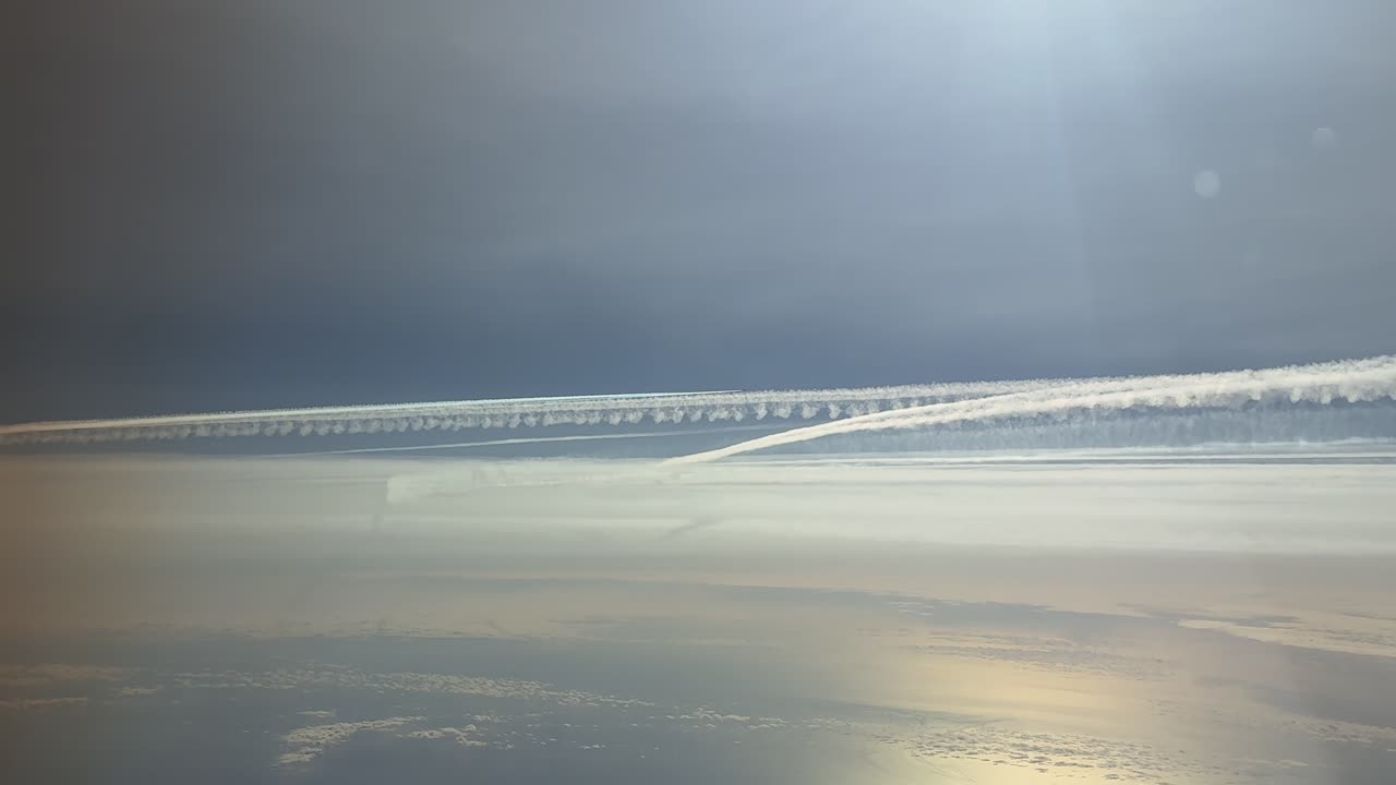 Luftfoto av parallelle kondensstriper i stratosfæren, fanget fra et jetflys cockpit på en solrik og lys dag.