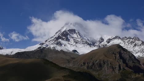 el monte kazbek o kazbegi está cubierto de nieve. el viento sopla nieve desde la cima de la montaña. stepantsminda, georgia