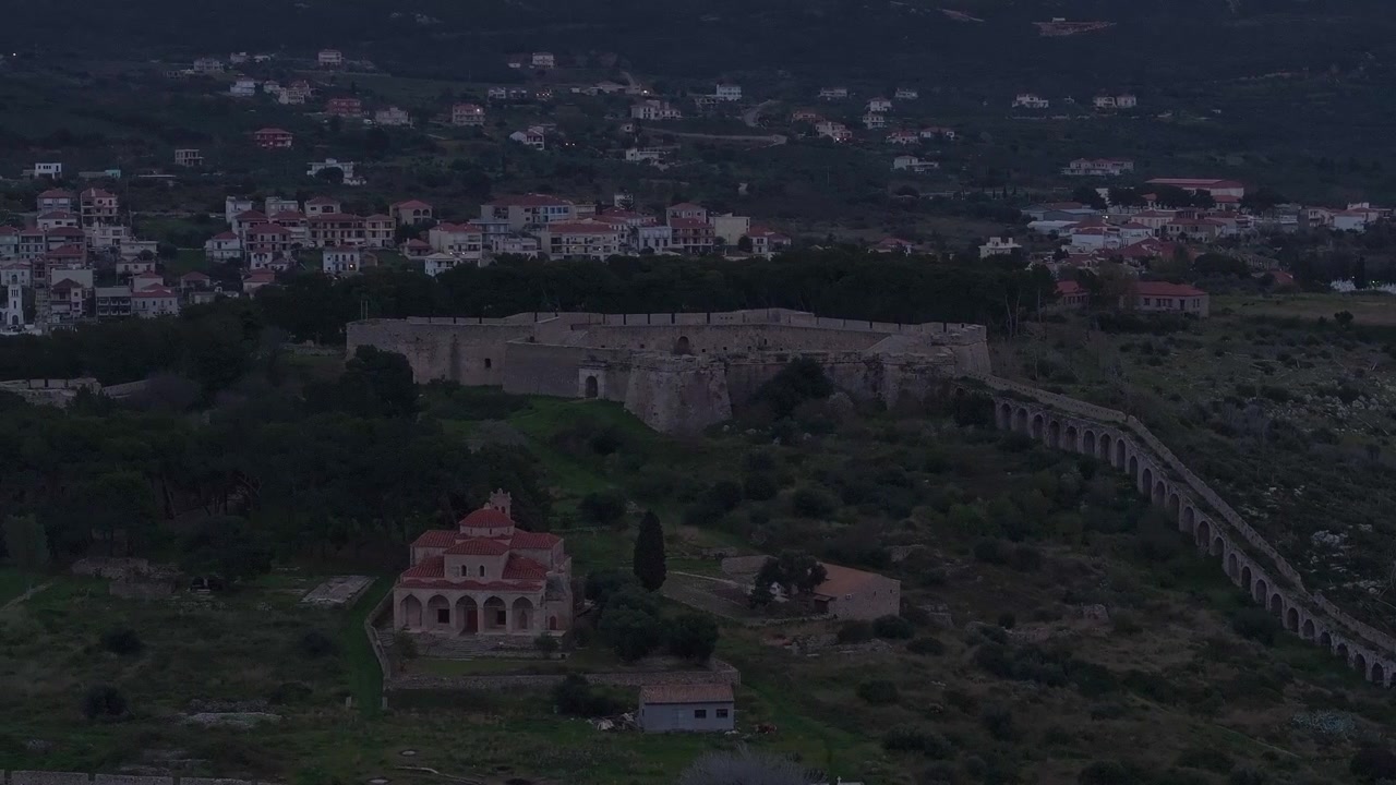 Veduta aerea del Castello di Niokastro, della Chiesa della Trasfigurazione e dell'antico acquedotto a Pylos, Grecia, sotto un cielo crepuscolare scuro e suggestivo con le luci della città in lontananza