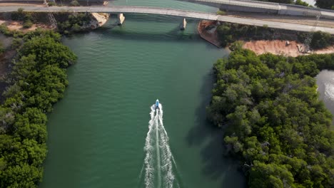 a speeding boat on an estuarine river seen from a bird's eye view speeding so fast going under two bridges also the drone reveals mangrove forests on both sides, porlamar, margarita island, venezuela