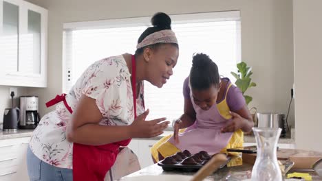 Happy-unaltered-african-american-mother-and-daughter-baking,-with-cakes-out-of-oven,-in-slow-motion