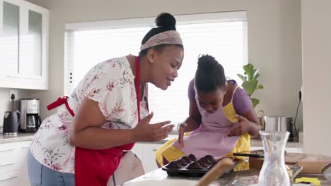 happy unaltered african american mother and daughter baking, with cakes out of oven, in slow motion