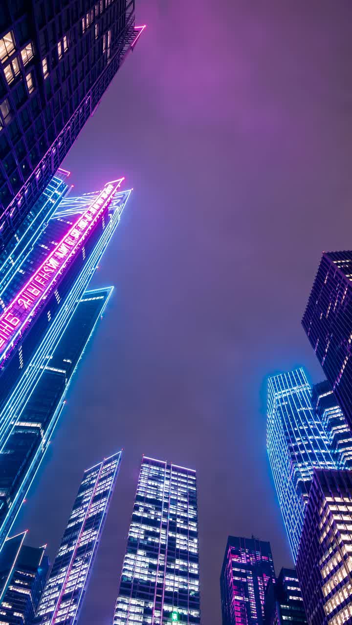 A futuristic cityscape with neon-lit skyscrapers shot from a low angle, evoking a cyberpunk video
