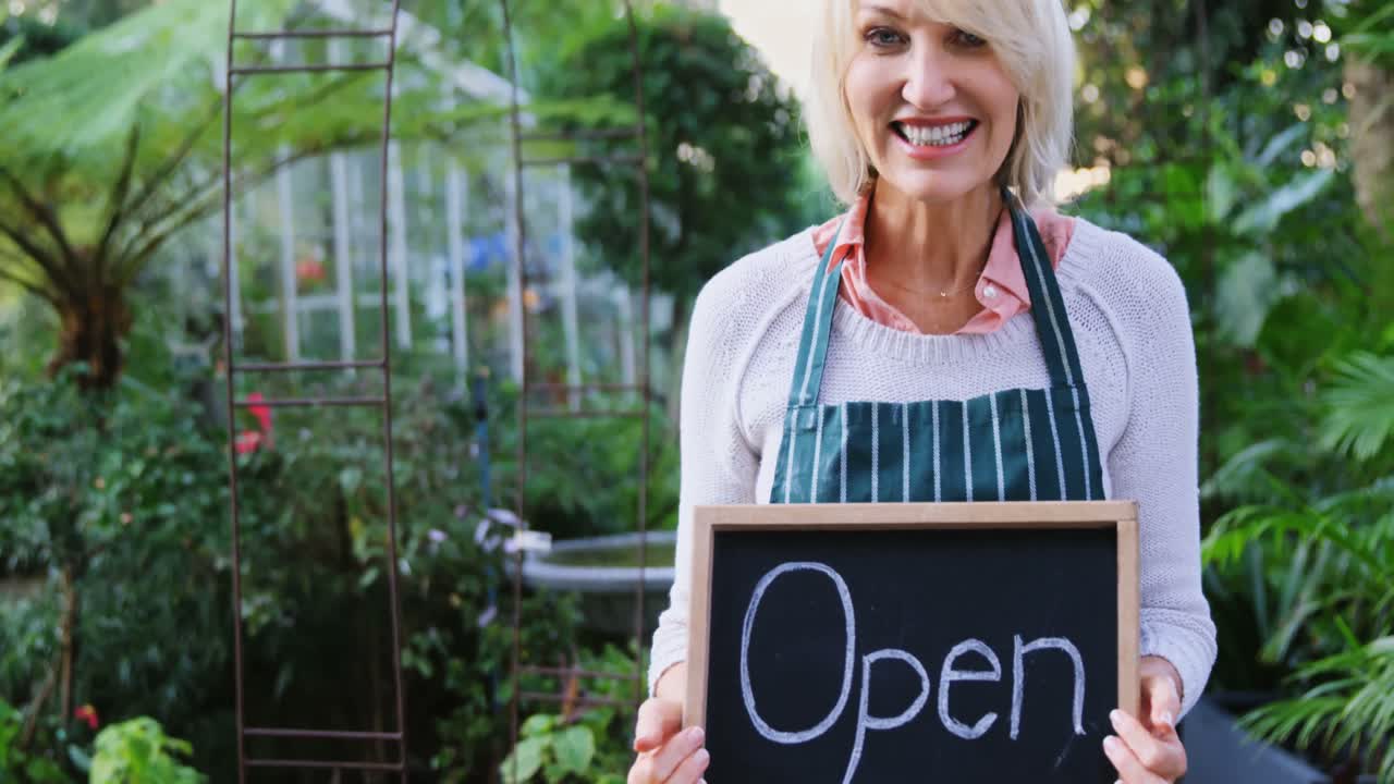 열려 있는 표지판 을 들고 있는 성숙 한 여자