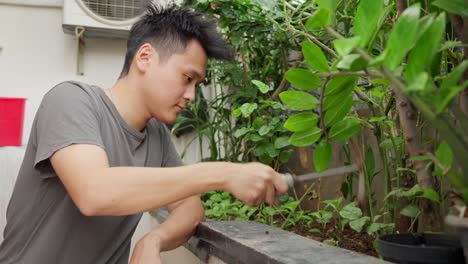 young asian man using garden shovel to dig soil