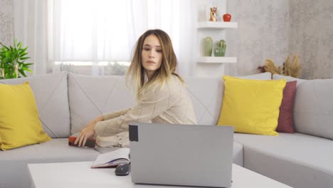 una joven estudiante estudiando en casa con una computadora portátil.