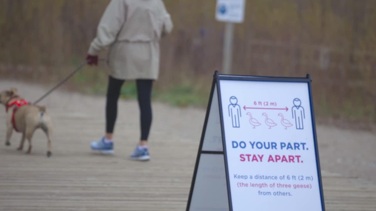 Woman Walking Her Dog At The Park In Canada, Passing By The Social Distancing Sign At The Entrance - slowmo