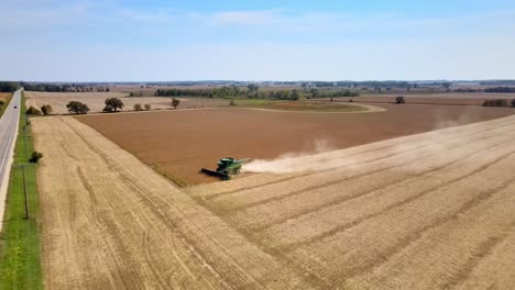 aerial view of a combine harvester tractor working on a grain farm during harvest season wisconsin - drone shot