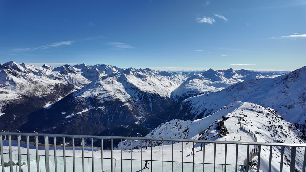 Wide panoramic winter landscape of the ski resort in Sölden, Austria, captured under bright alpine sunshine. The image shows a high-altitude glacier slope in the Ötztal Alps with ski lifts