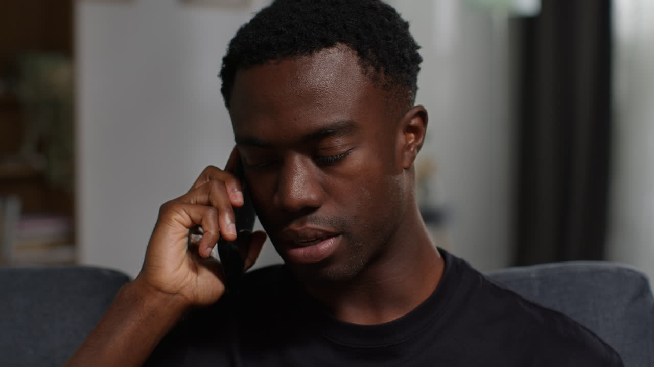 Unhappy And Depressed Young Man Sitting On Sofa At Home Ending Call After Talking On Mobile Phone