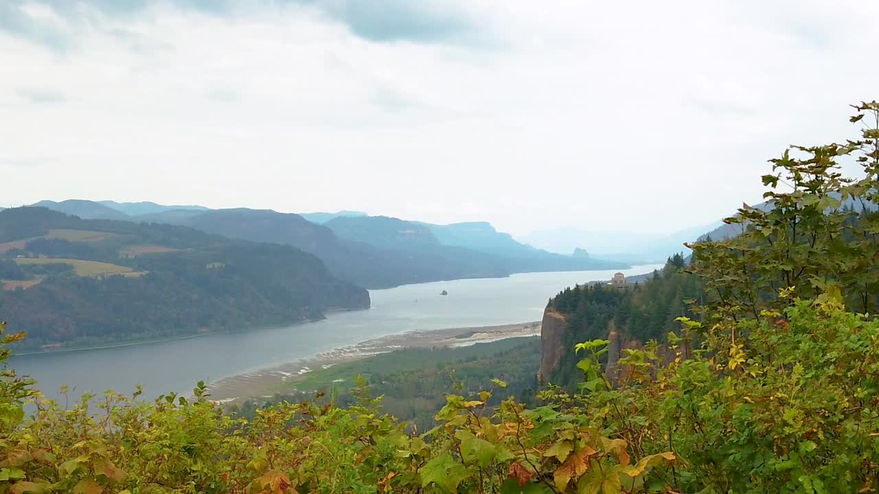 HD Boom up with autumn colored hedges in foreground and the Vista House on a cliff in the distance overlooking the Columbia River with mostly cloudy sky take four