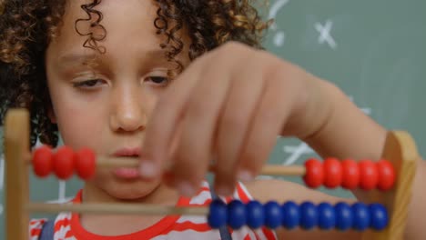 vista frontal de una colegiala de raza mixta aprendiendo matemáticas con ábaco en un aula de la escuela 4k