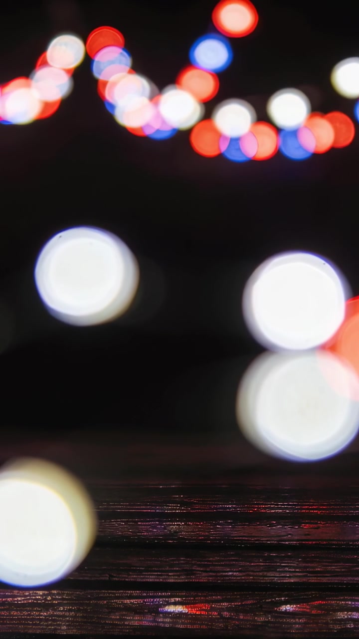 Vertical video: Gentle motion making string lights shimmer over wood tabletop, producing bokeh