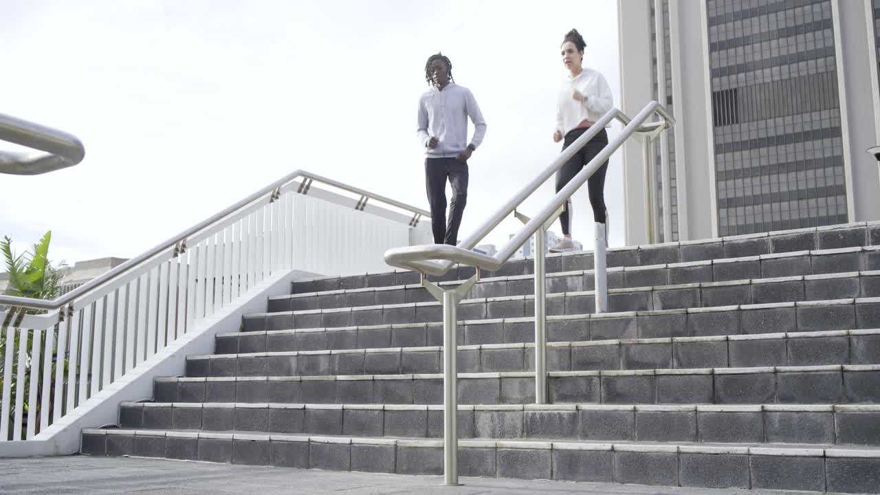 Starting workout atop urban staircase, diverse friends jogging down and sprinting up by handrail