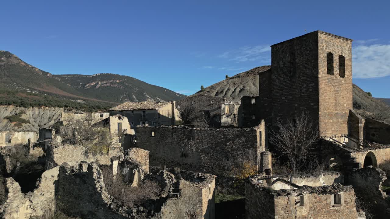 Rovine desolate del villaggio medievale abbandonato di Esco in Aragona, Spagna, che mostrano i resti di antiche case in pietra e una storica torre campanaria sullo sfondo di colline brulle