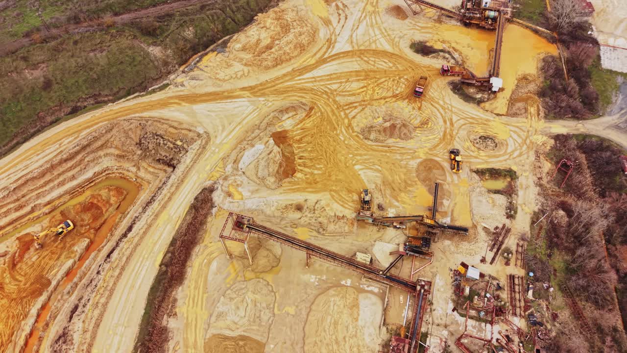 Sand quarry area with heavy machinery and dirt paths in sunlight