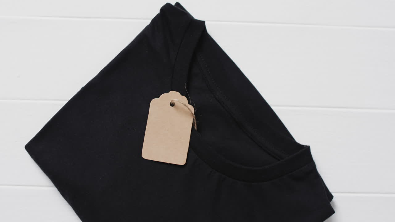 Video of flat lay of black t shirt with tag and copy space on white background