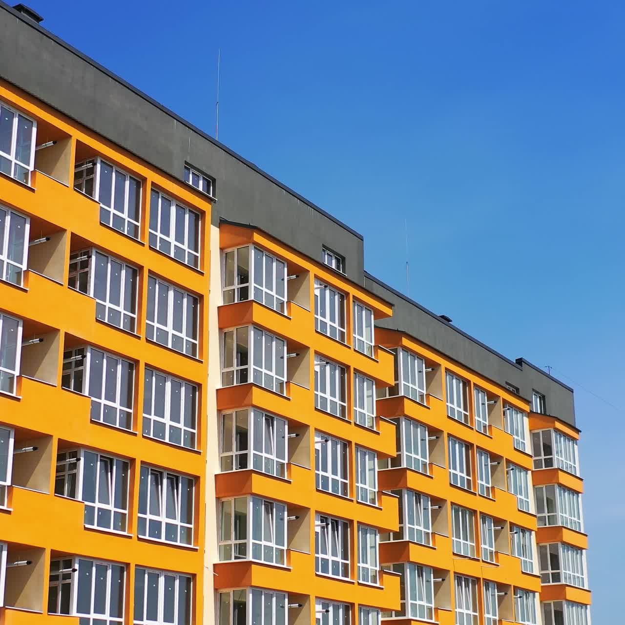 Modern high-rise building against blue sky. Newly built apartment building with colorful walls for urban residents. Bright facade of multi storey city house