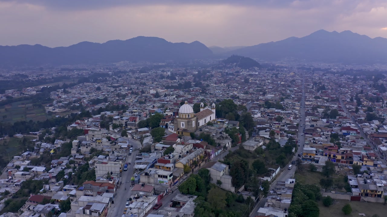 An aerial drone shot captures the charming colonial city of San Cristóbal de las Casas in Chiapas, Mexico, at sunset.