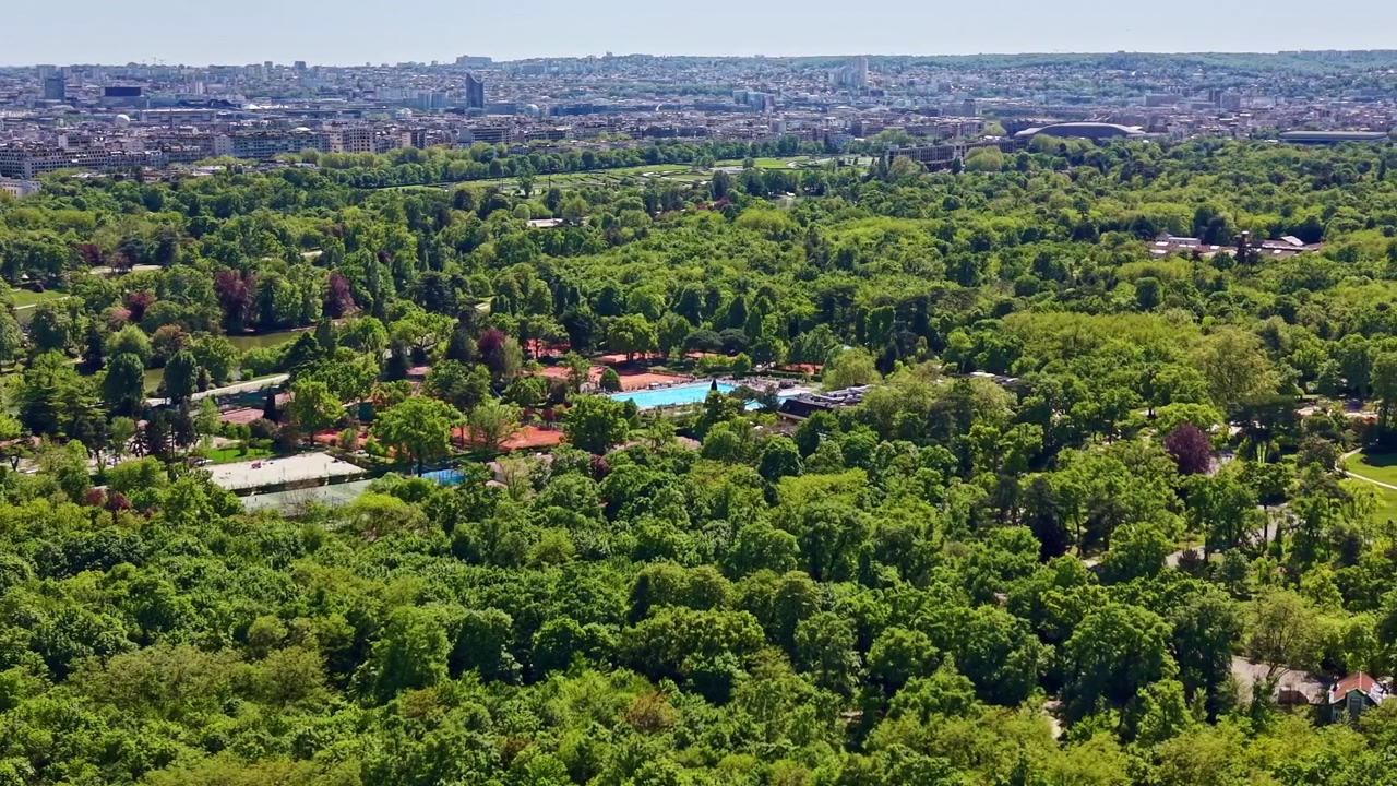 Le drone survole les courts de tennis en terre battue et la piscine du Bois de Boulogne, avec la ligne d'horizon de Paris en arrière-plan.