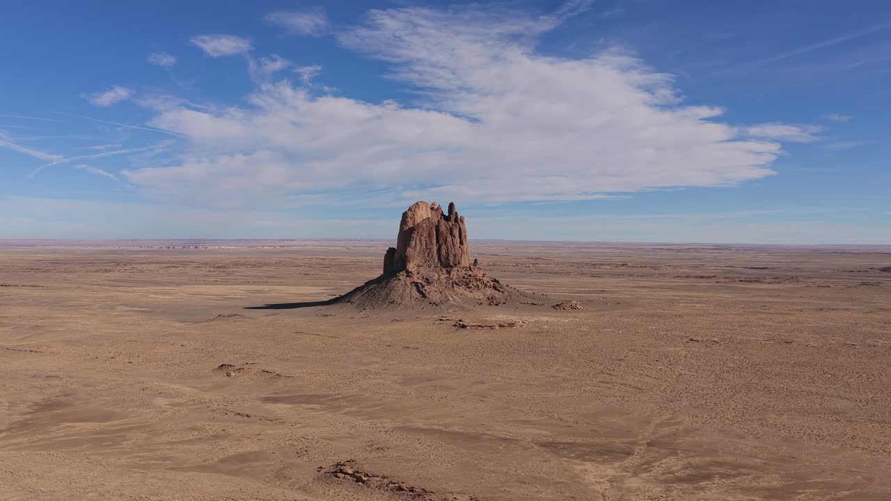 Dronevlucht benadrukt de ruwe textuurpatronen en de enorme schaal van een geërodeerde zandsteenrotsmonoliet die oprijst uit een vlak, dor woestijnplateau in de afgelegen hoge woestijn.