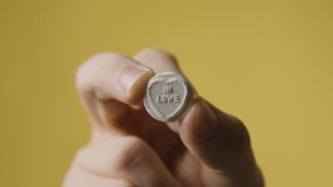 close up of hand holding heart candy with in love message on yellow background