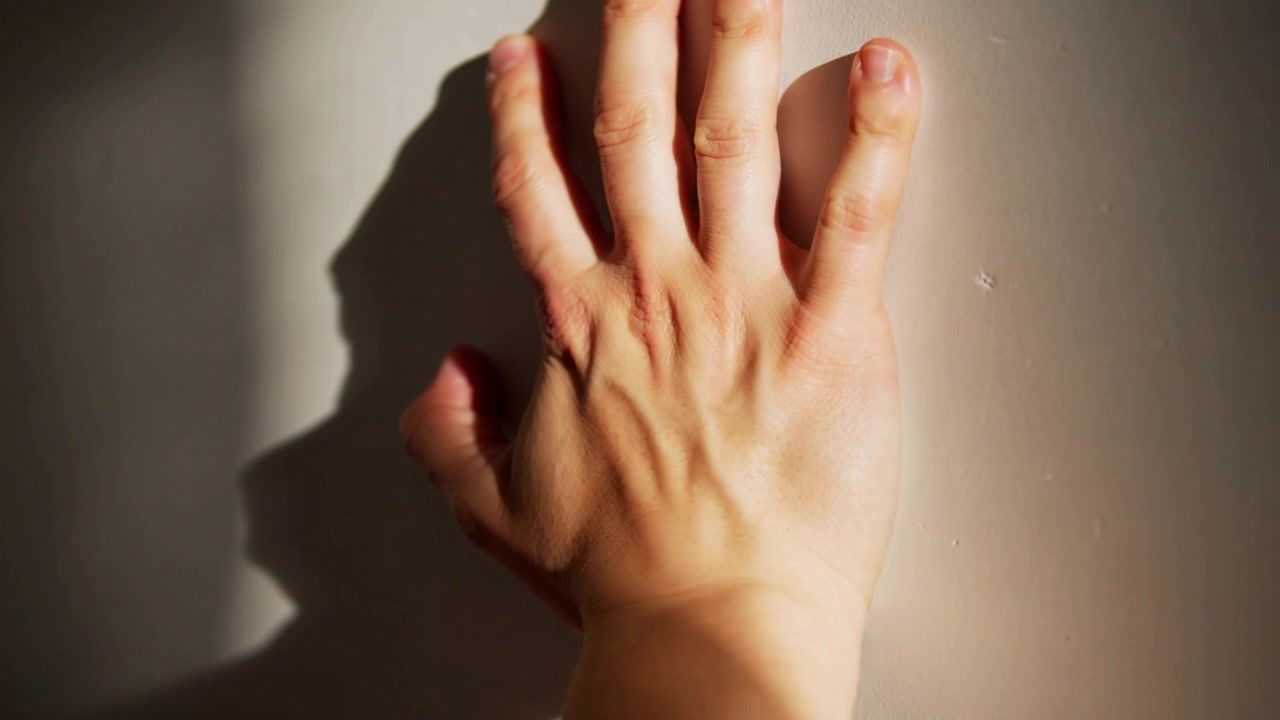 Pressing hand adjusting fingers on wall, warm light sharpening shadow and showing droplets right