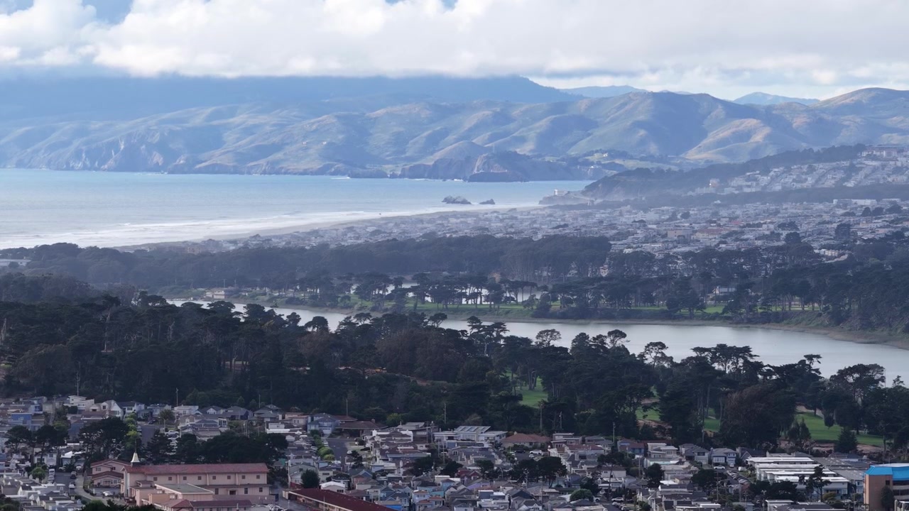 北カリフォルニアの海岸沿い、オーシャンビーチとマーセド湖を見下ろすデイリーシティのなだらかな丘と密集した住宅街をドローンが捉えた景色。