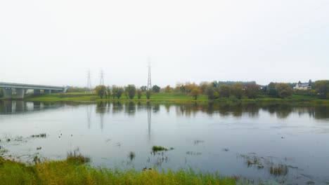 Drohnenaufnahme-Einer-Brücke-Mit-Fahrenden-Autos,-Die-Den-Neman-Fluss-überqueren,-Und-Sendemasten-Im-Hintergrund-In-Kaunas,-Litauen,-Während-Der-Morgenzeit