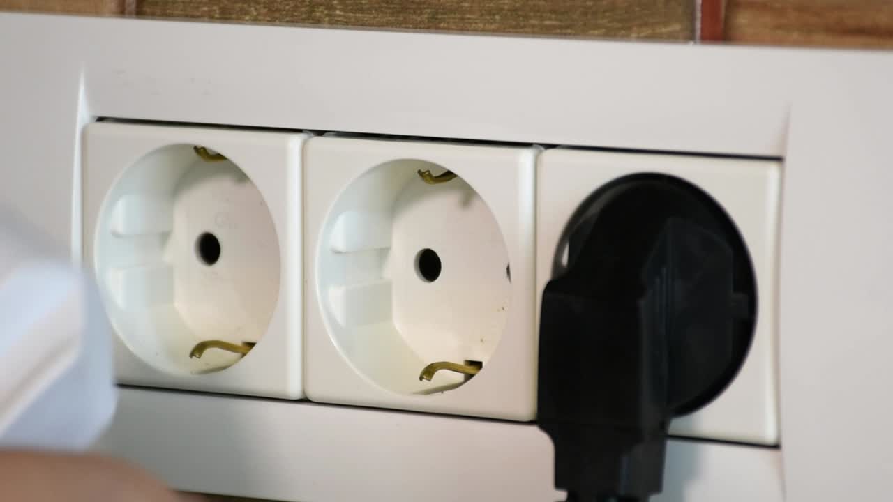 Woman inserts power cables into electrical wall socket