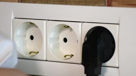una mujer inserta cables de alimentación en una toma de corriente