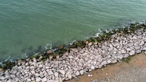 Aerial-birds-eye-view-above-splashing-ocean-tide-breaking-on-rocky-coastal-shoreline-rotating-left