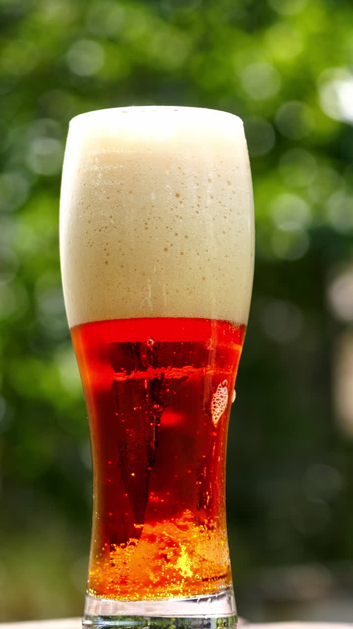 Glass of beer stands on a summer terrace. Full glass of dark beer with foam and small bubbles inside. Close-up. Vertical video