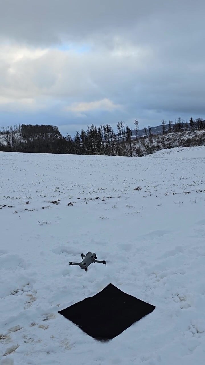 Modern quadcopter with a camera taking off from a landing pad in a snowy winter landscape