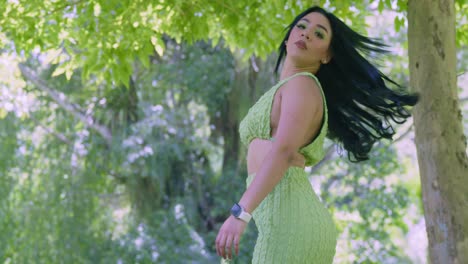 a young walks away in a short and tight green dress before turing around with her hair flowing in the wind