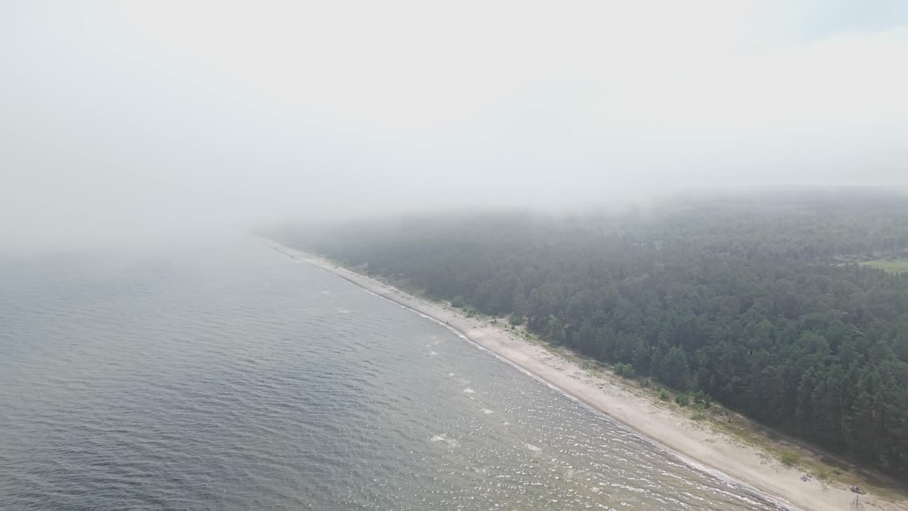 Aerial of coastline beneath low clouds, road follows shoreline under foggy sky