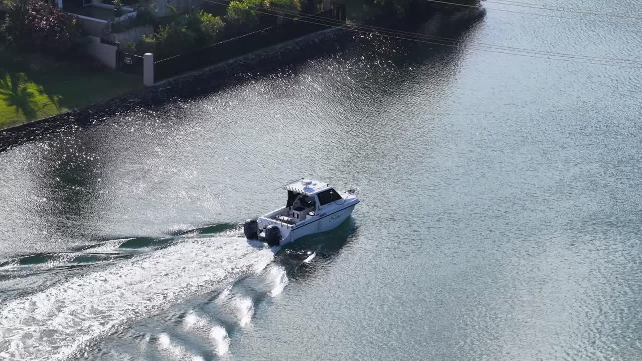 A motorboat travels smoothly along a residential canal on the Nerang River, Gold Coast, Australia. Aerial view with bright daylight and gentle water reflections