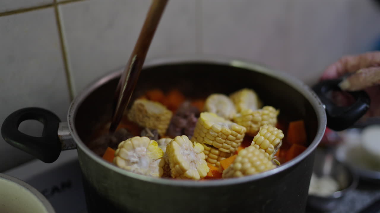 Colorful vegetables simmer in a pot on the stove, preparing traditional Argentine Locro.