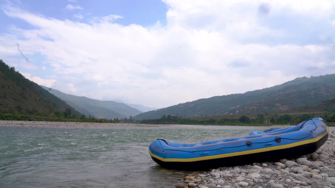Una zattera è adagiata sulle rocce vicino al fiume Pho Chu Mo Chu a Punakha, Bhutan, e l'acqua scorre con vista sulle montagne.
