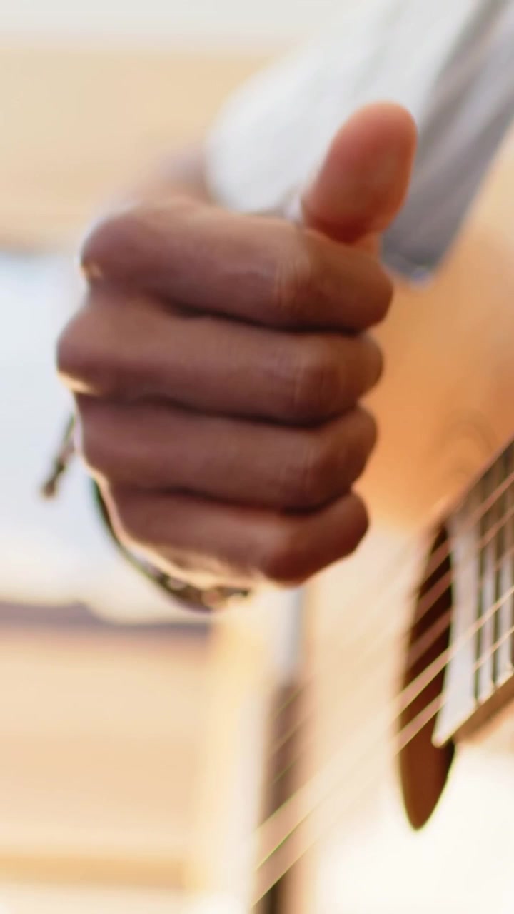 Video verticale: Messa a fuoco su un uomo che pizzica le corde di una chitarra acustica, strimpellando con il pollice, mentre si esercita a casa.