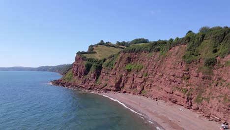 vuelo aéreo hacia adelante a lo largo de la playa de ness cove y el acantilado de arcilla roja en shaldon, south devon, inglaterra