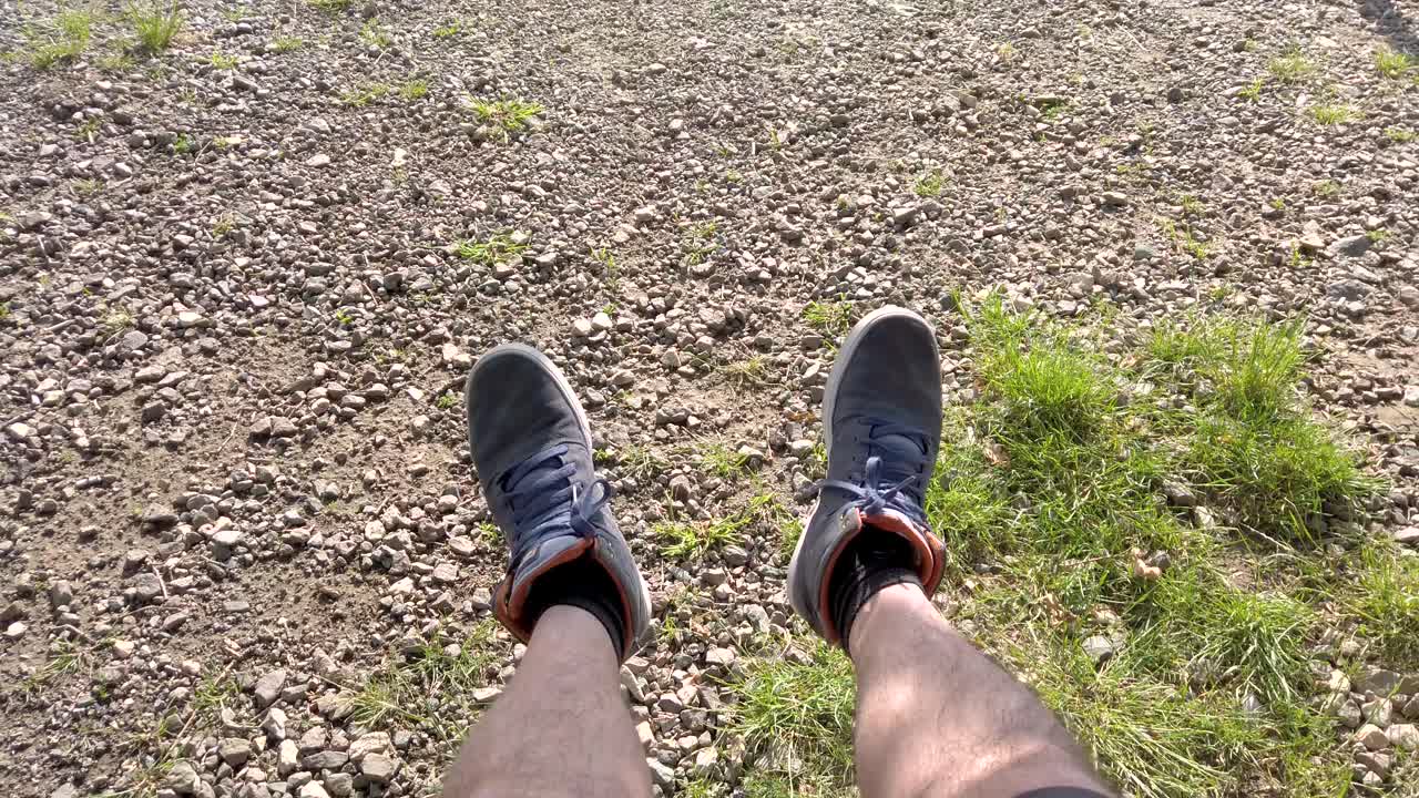 Legs and shoes of a swinging man. Gravel and green grass around. Outdoor relaxing on a sunny day.