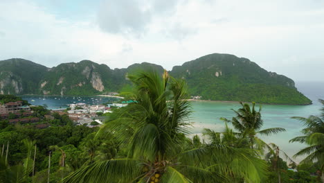 revealing drone shot of phi phi island bay with tropical mountains during cloudy day above palm trees, thailand