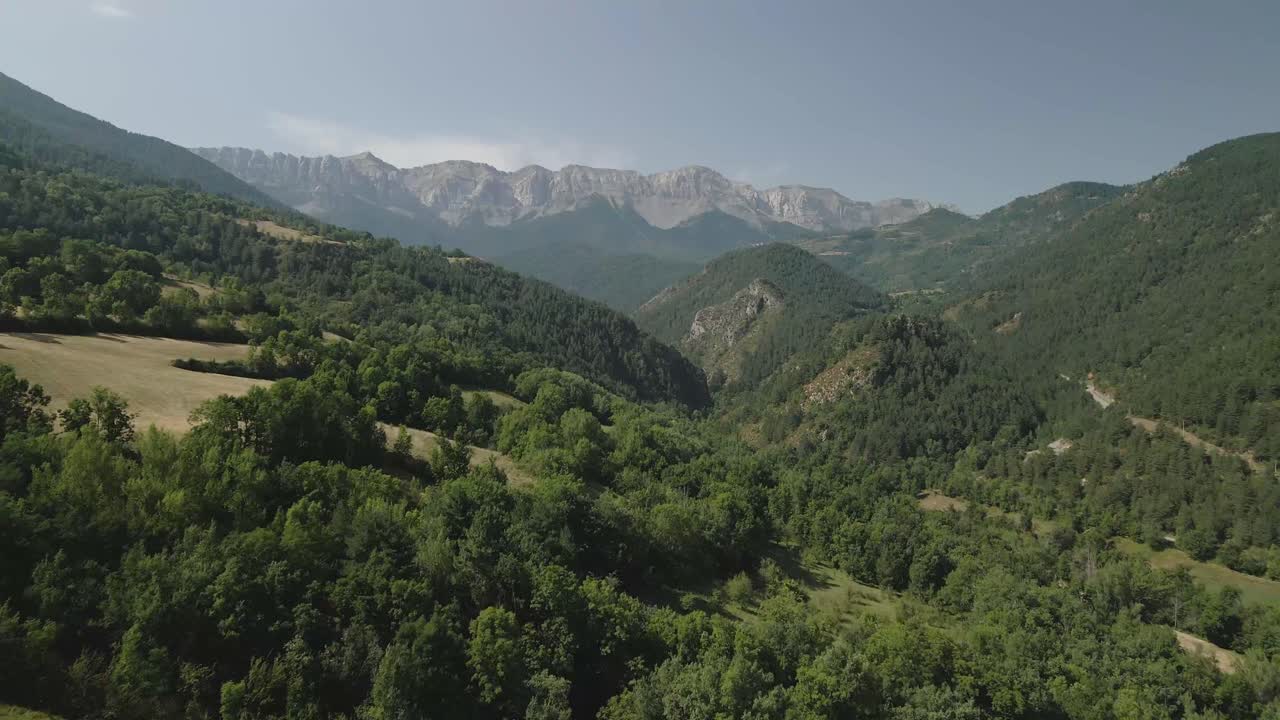 vista aérea de un dron que avanza entre montañas y sobre el bosque, con la cordillera de cadi en el horizonte