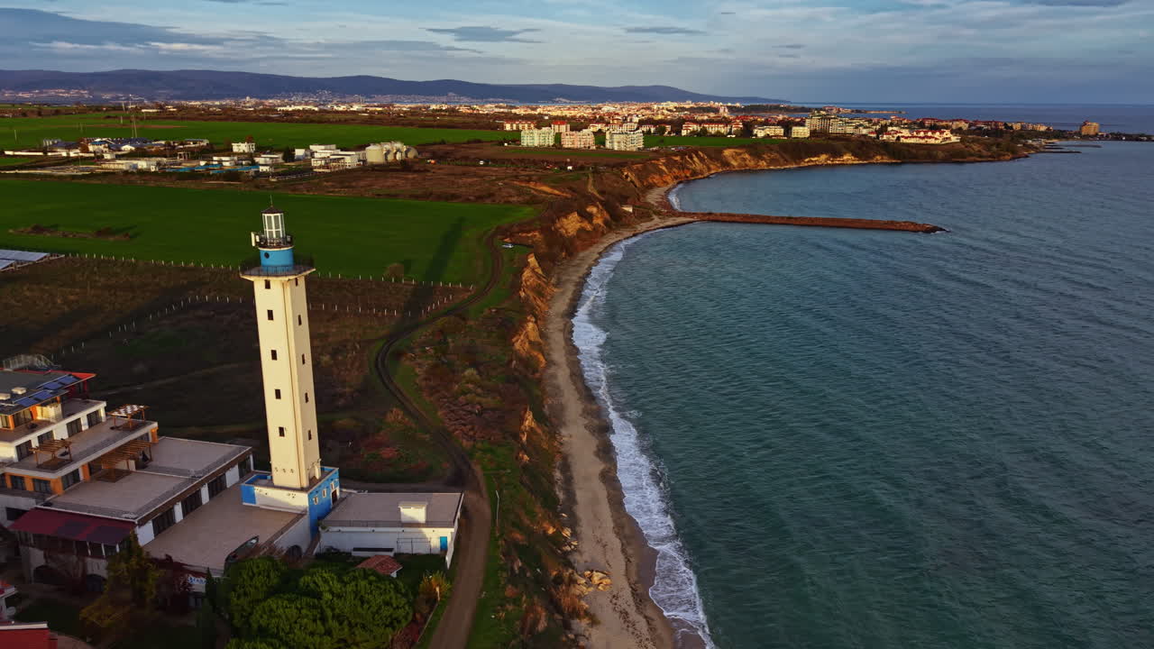 Panorama costiero con un faro che si erge in tutta la sua altezza accanto alle onde serene, catturando la bellezza del mare e del paesaggio al tramonto
