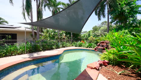 tropical pool on property with large rock water cascading feature in corner and sun canopy shade